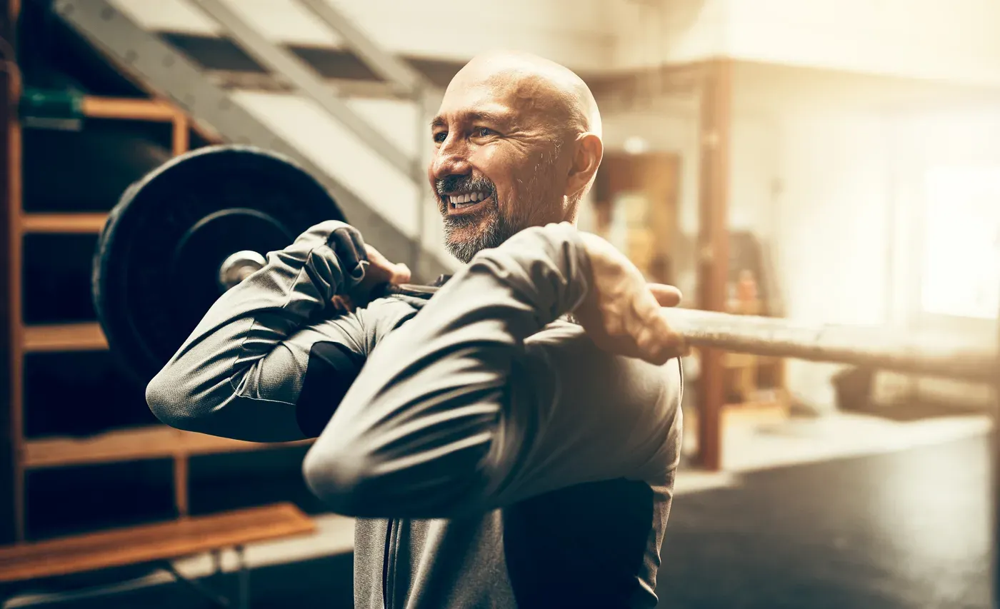 Smiling bald man holding a barbell in the front rack position