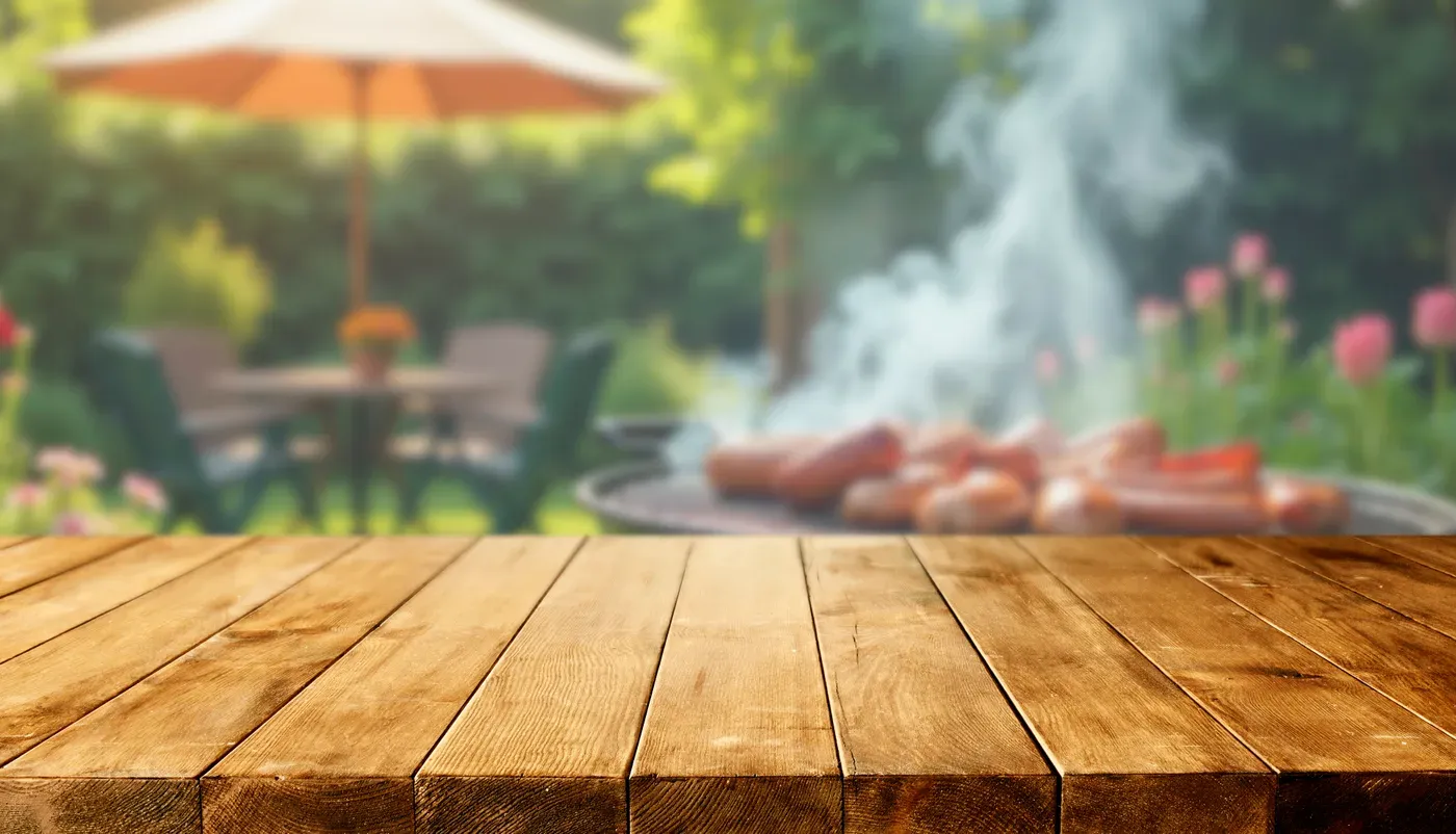 Wooden table in front of a smoking backyard barbecue grill with sausages