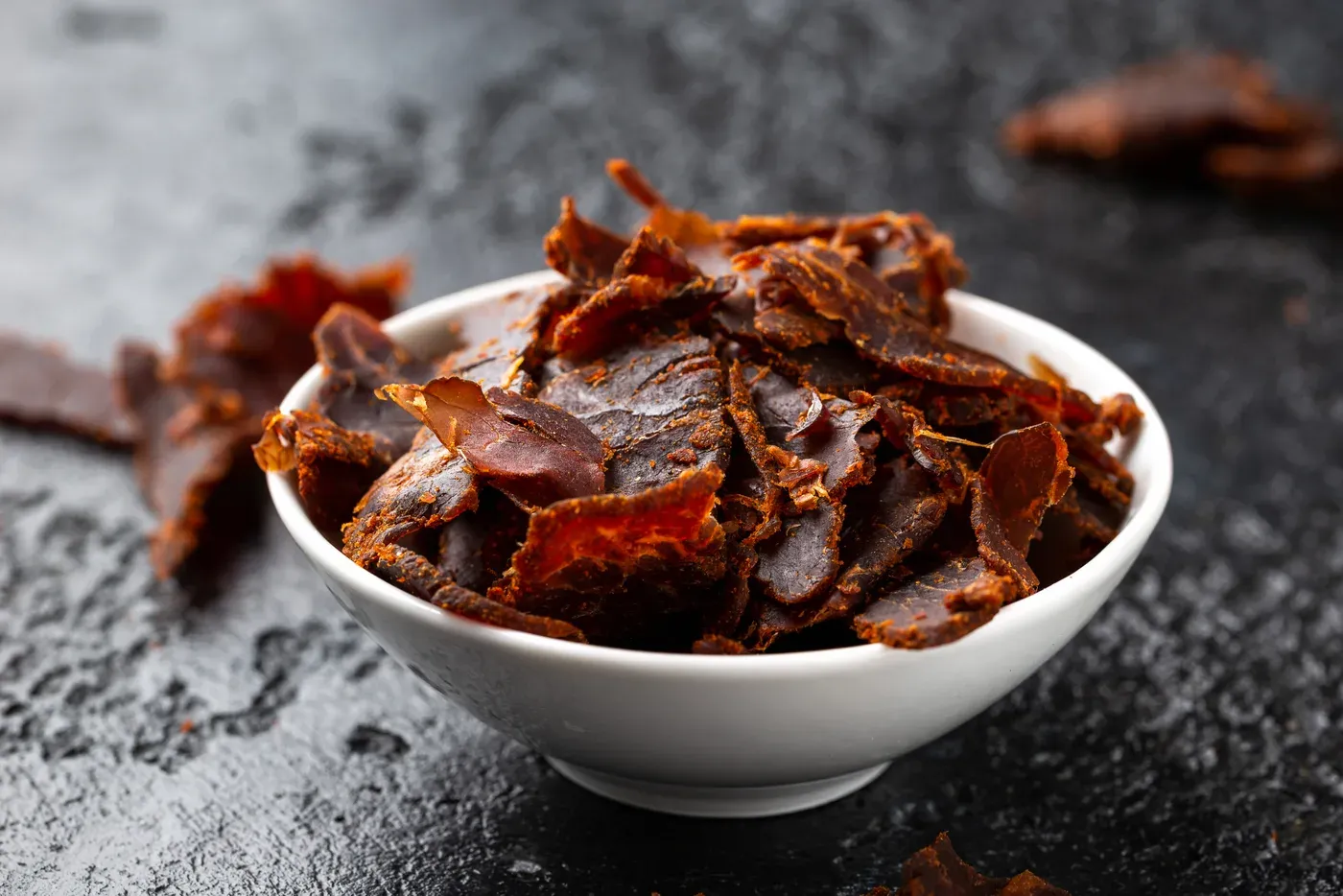 White bowl filled with dried beef jerky on a dark stone surface