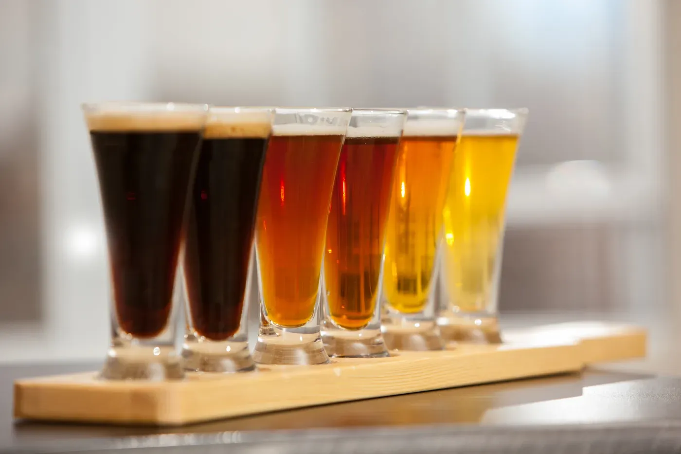 Six tasting glasses of beer from dark to light on a wooden paddle