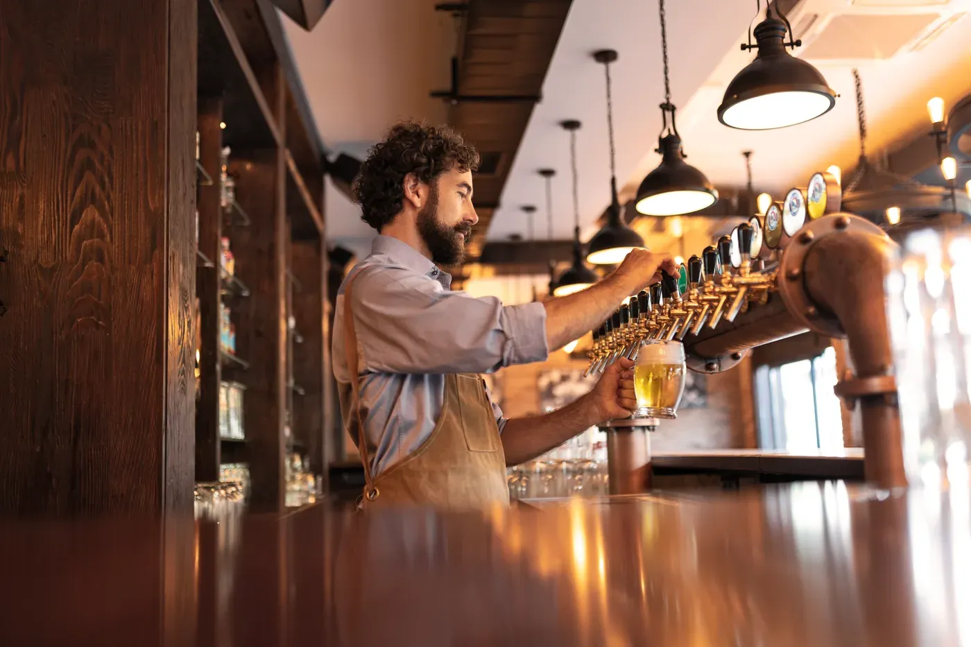 Bearded bartender pouring a pint of beer from a row of taps in a pub