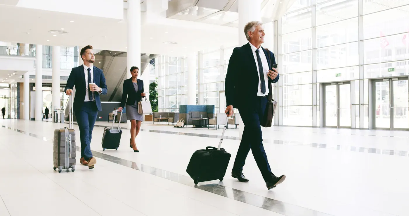 Businessmen in suits walking through an airport terminal pulling carry-on suitcases