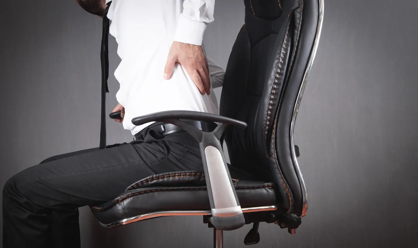 Man in a white shirt holding his lower back while sitting in an office chair