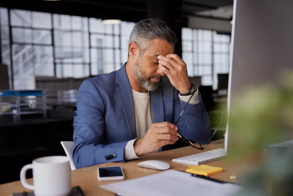 Tired professional in his forties rubbing his eyes at his desk