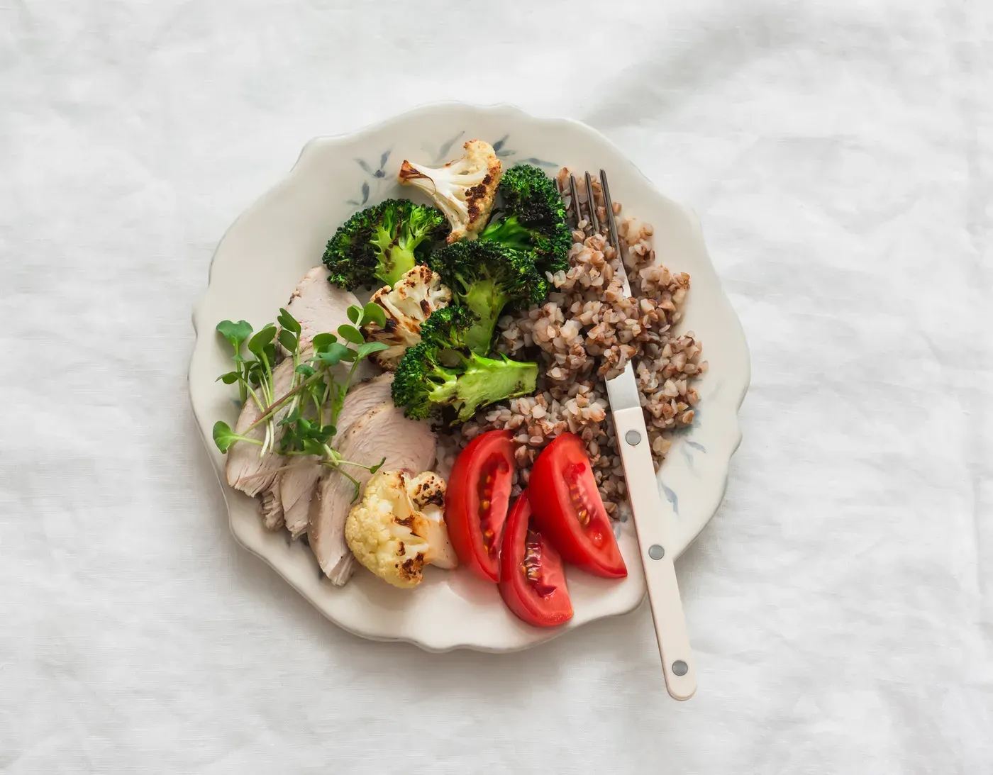 Plate of sliced chicken breast, roasted broccoli, cauliflower, buckwheat and tomatoes