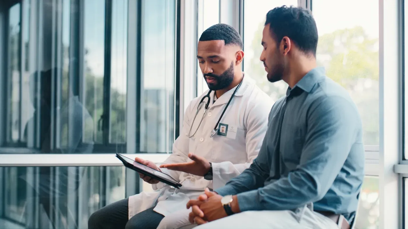 Doctor in a white coat reviewing results on a tablet with a male patient