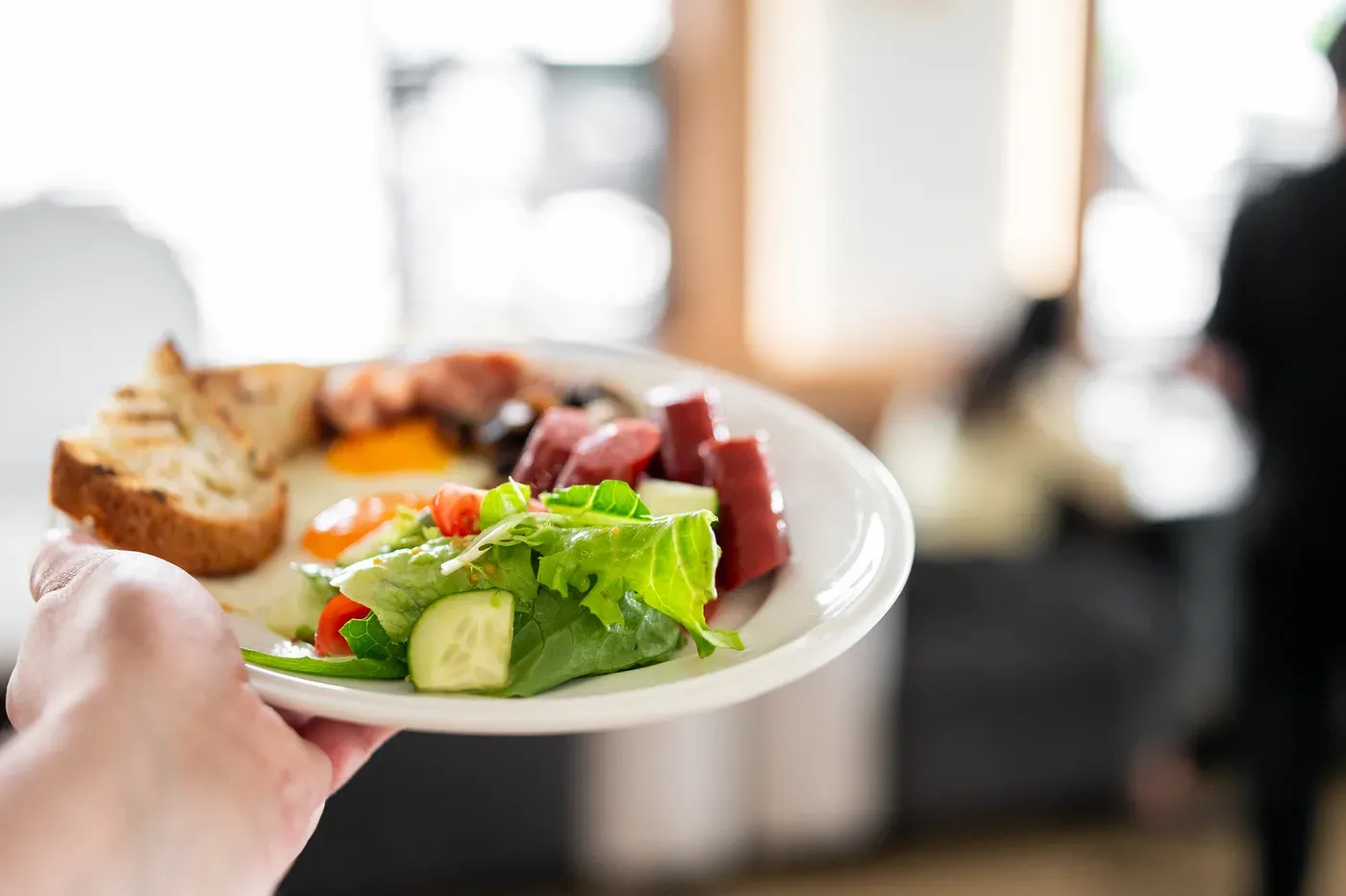 Hand holding a plate of fried egg, toast, salad and sliced meat