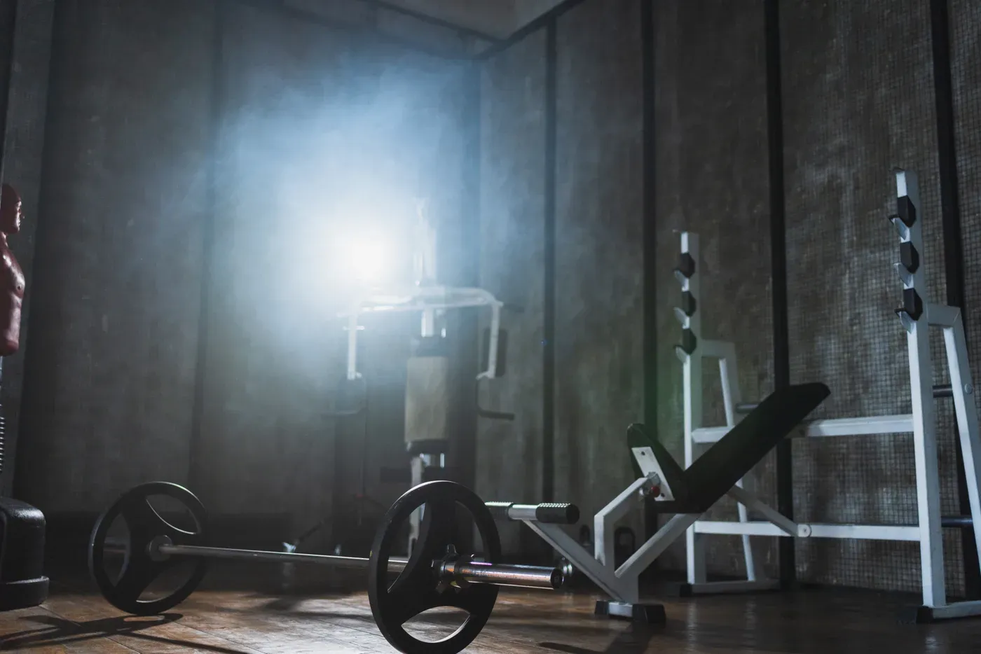 Dark home gym with a loaded barbell, weight bench and squat rack