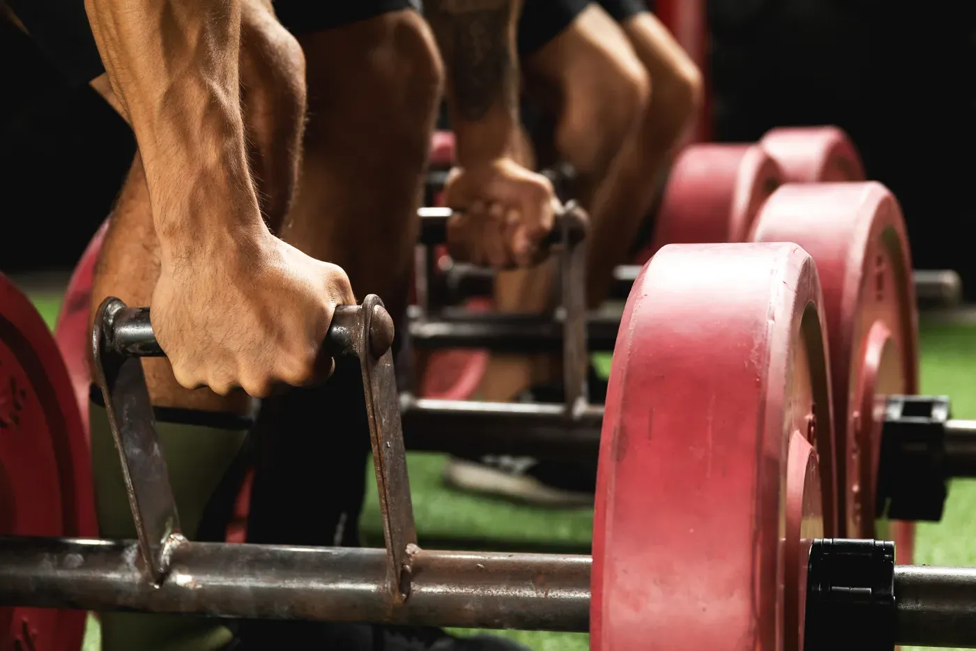 Close-up of hands gripping farmer’s walk handles loaded with red plates