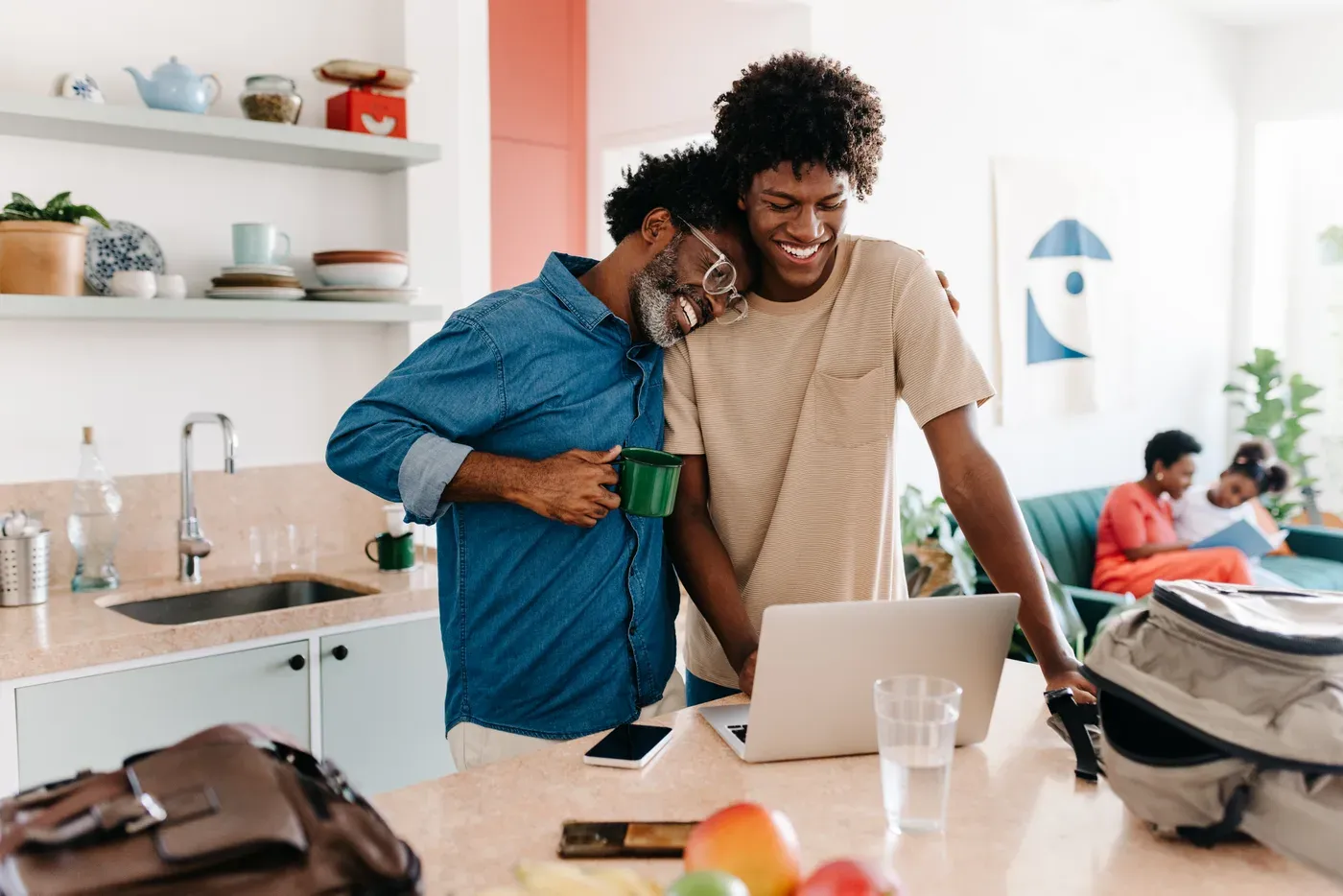 Father hugging his adult son while they look at a laptop in the kitchen