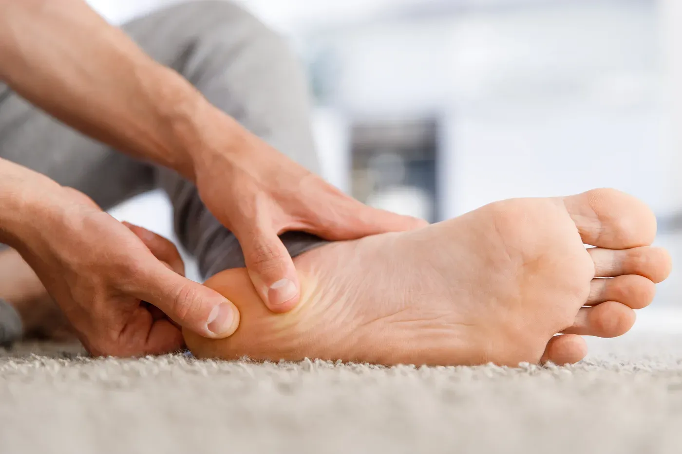 Man massaging the sole of his bare foot while sitting on a carpet
