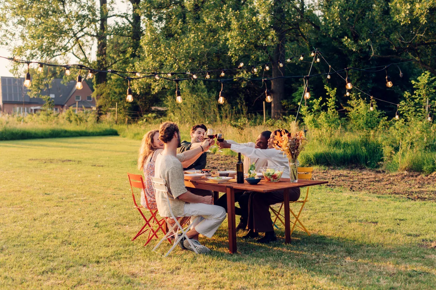 Group of friends toasting at a long dinner table in a backyard under string lights