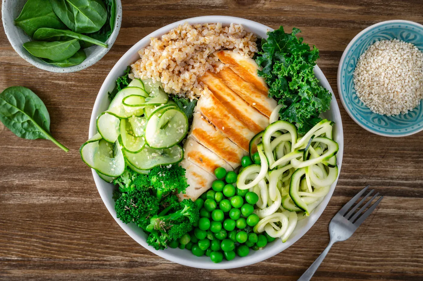 Bowl of sliced grilled chicken with grains, peas, broccoli, cucumber and zucchini