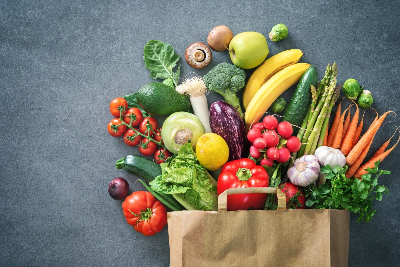 Fresh vegetables and fruit spilling out of a paper grocery bag