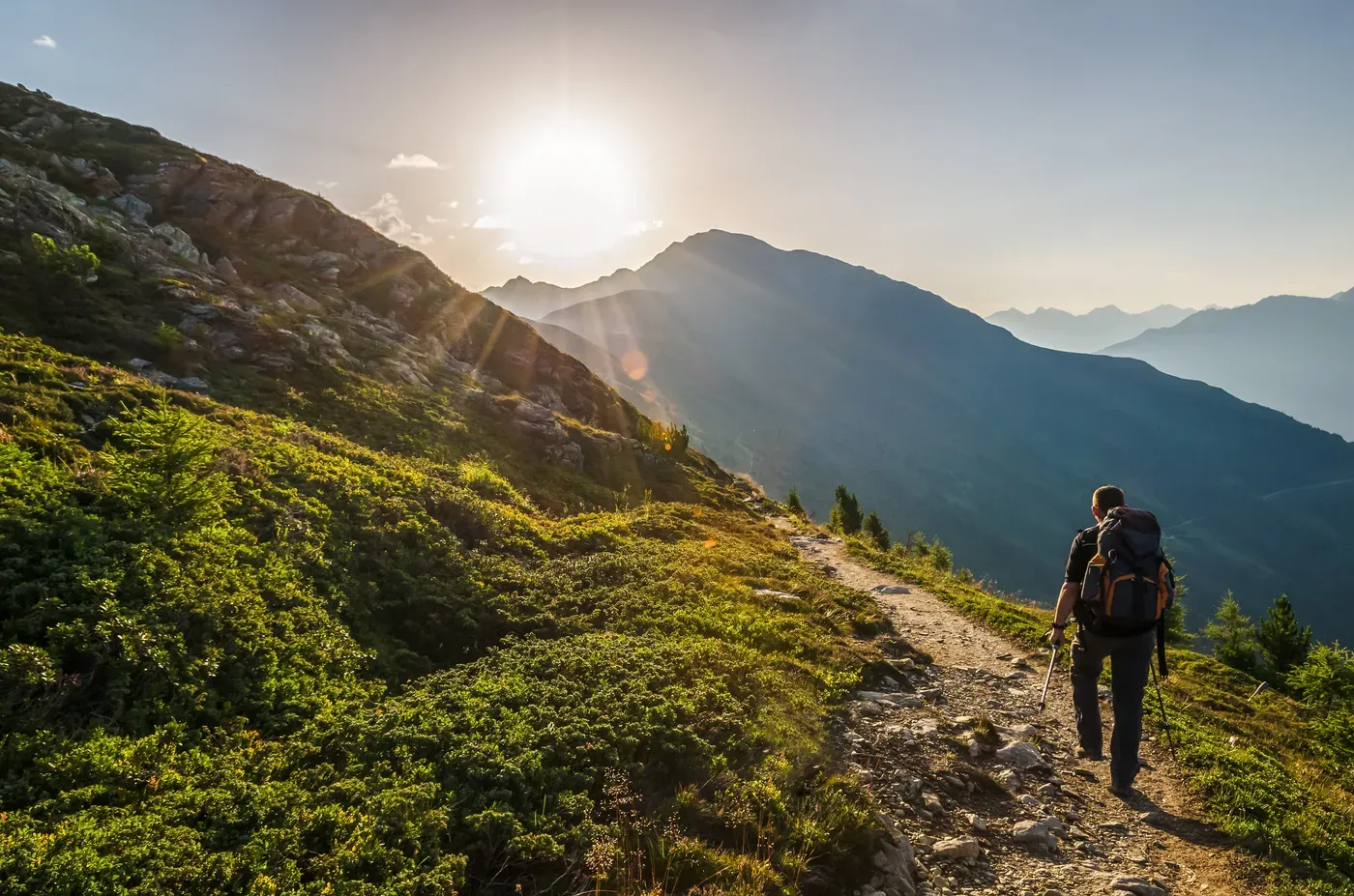 Hiker with poles and a backpack on a mountain trail at sunrise