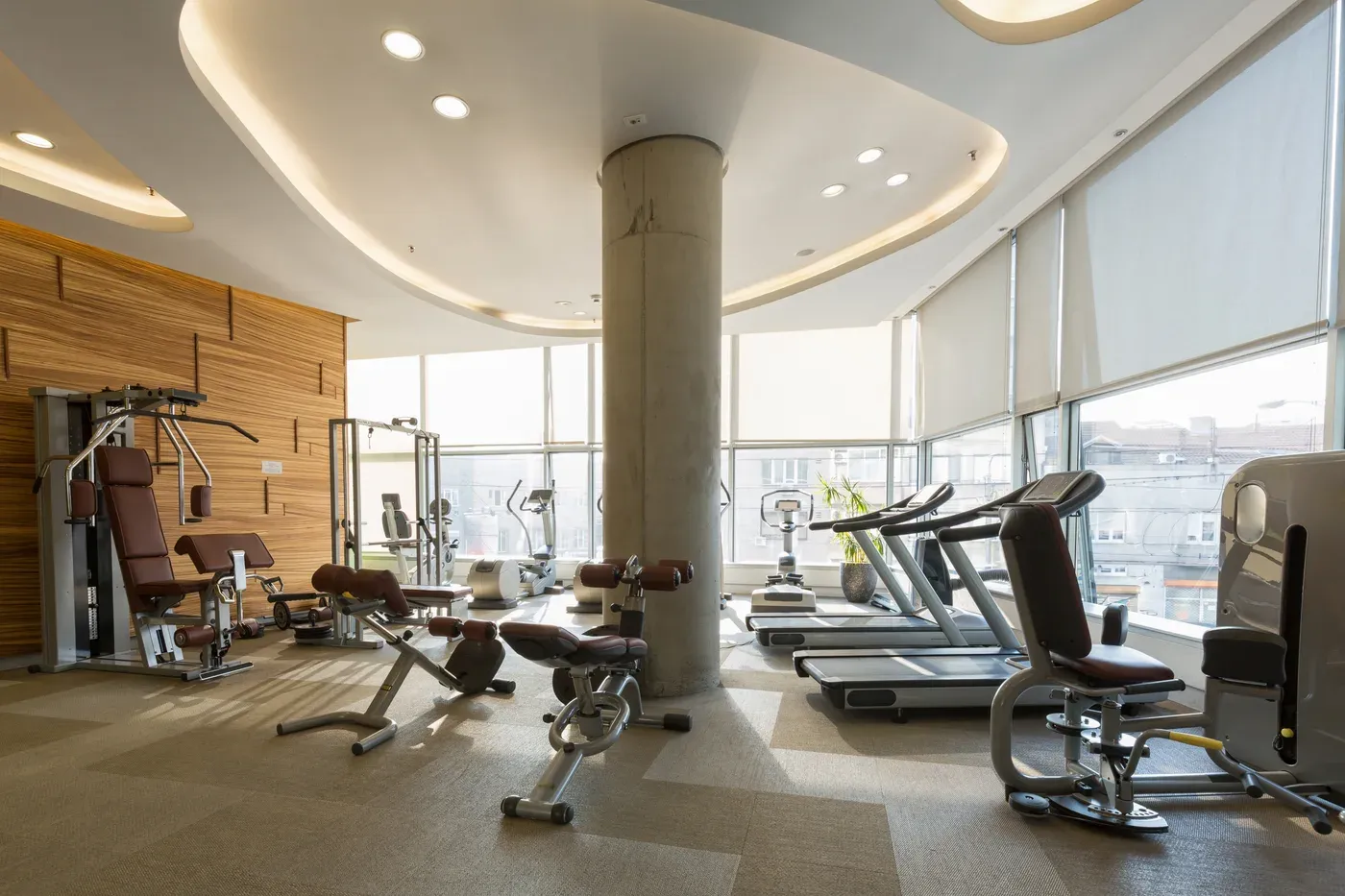 Bright, empty hotel gym with treadmills and weight machines by the windows