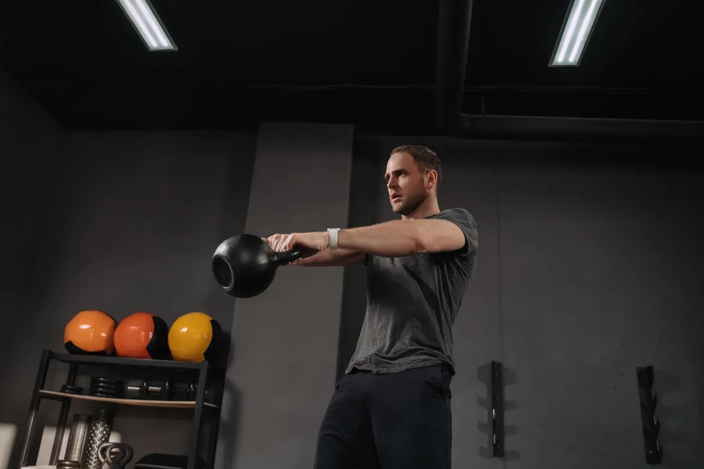 Man swinging a kettlebell to chest height in a dark gym