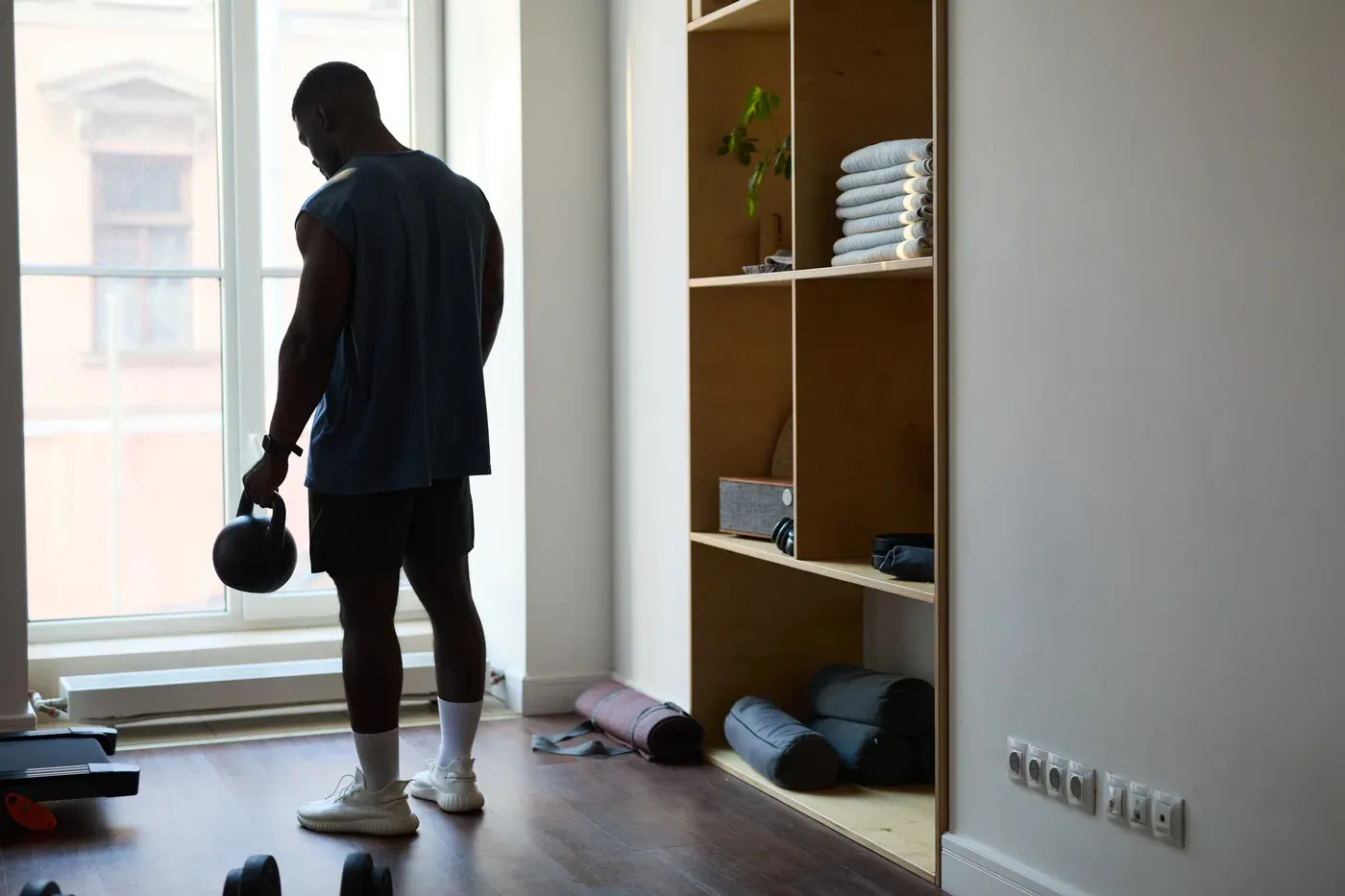 Man holding a kettlebell in a minimalist home workout room by a window