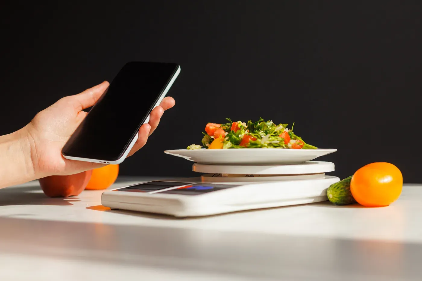 Hand holding a phone beside a salad being weighed on a kitchen scale