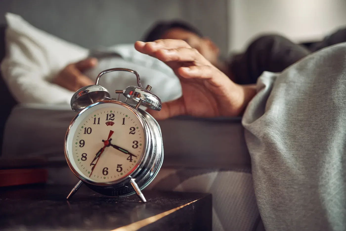 Man in bed reaching for a ringing alarm clock on the nightstand