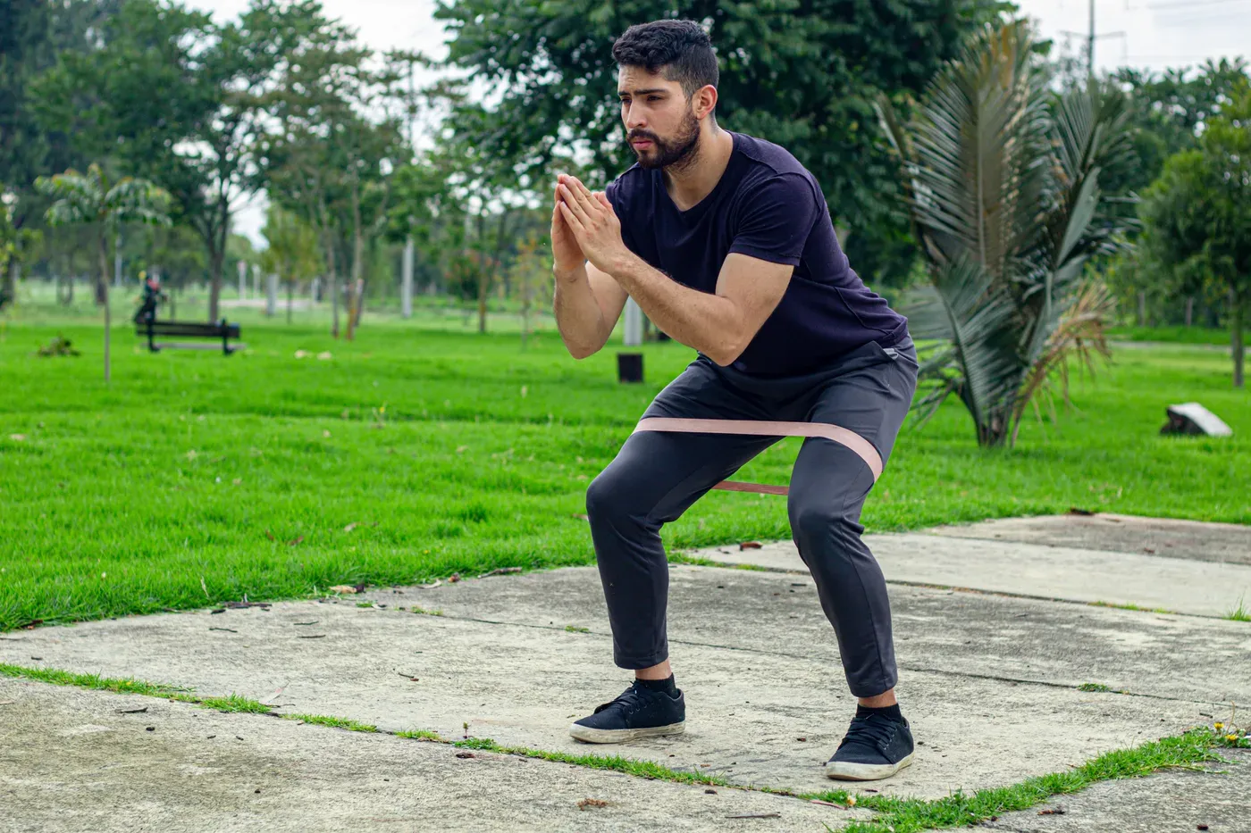 Bearded man doing a banded squat on a park path