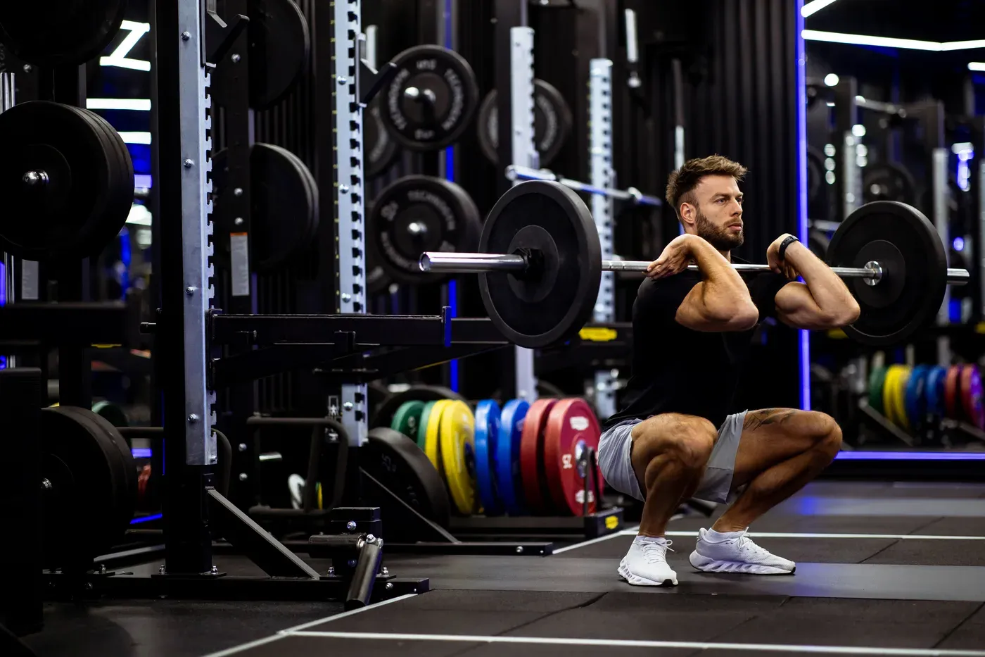 Bearded man holding a deep barbell front squat in a modern gym