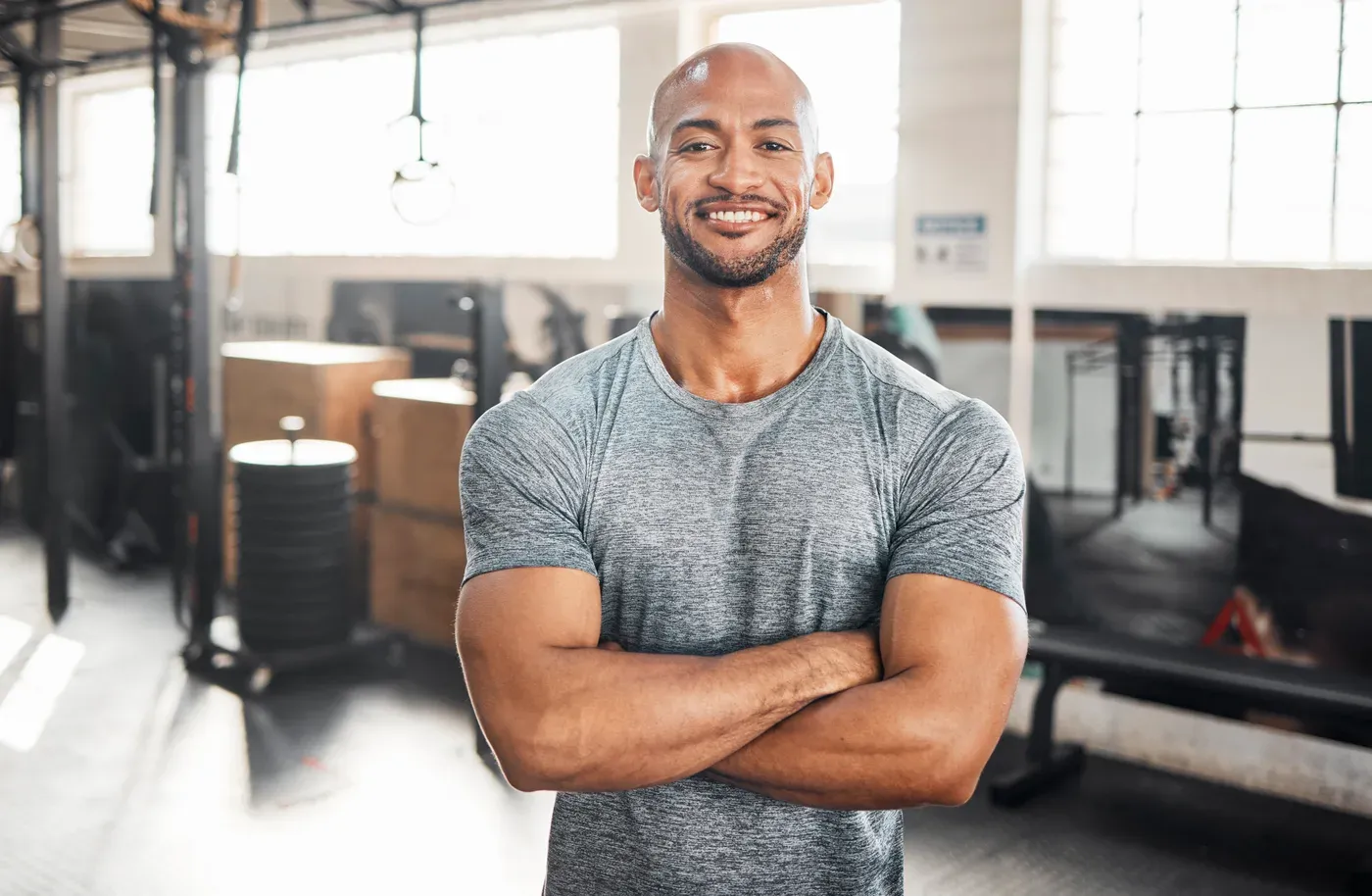 Smiling bald man with folded arms standing in a gym