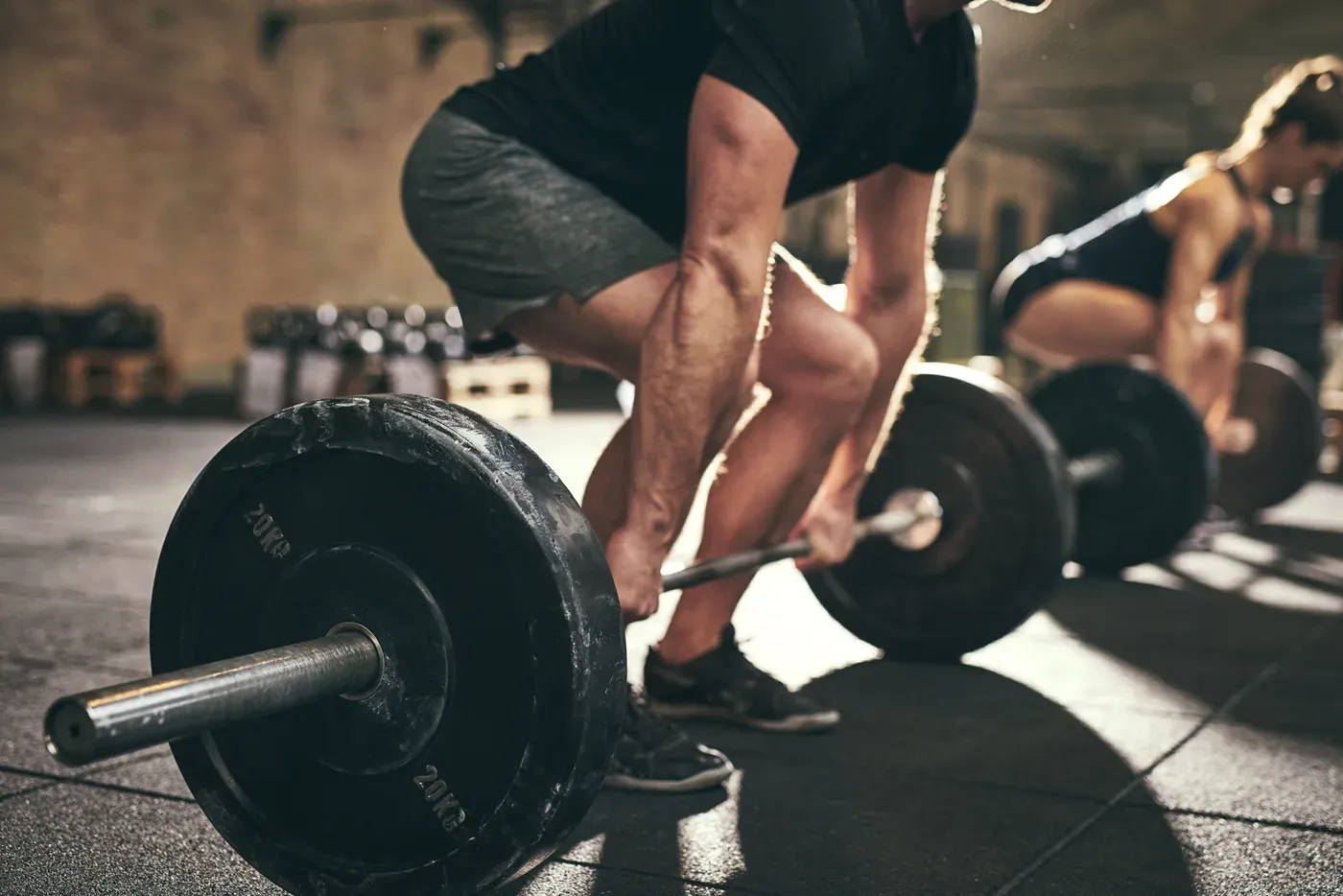 Man gripping a loaded barbell for a deadlift, another lifter behind