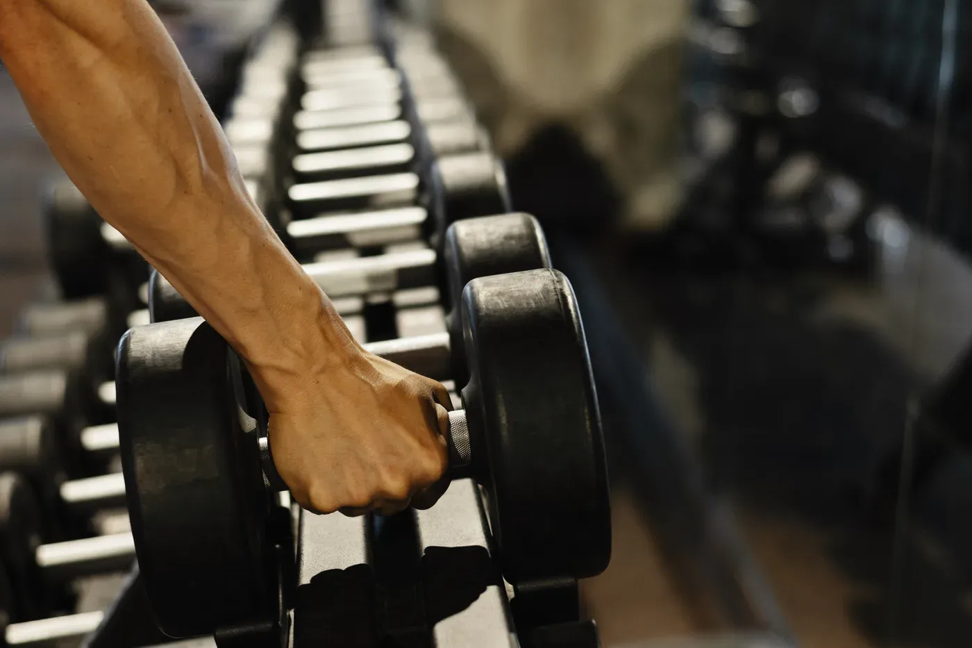 Close-up of a hand lifting a dumbbell from a gym rack
