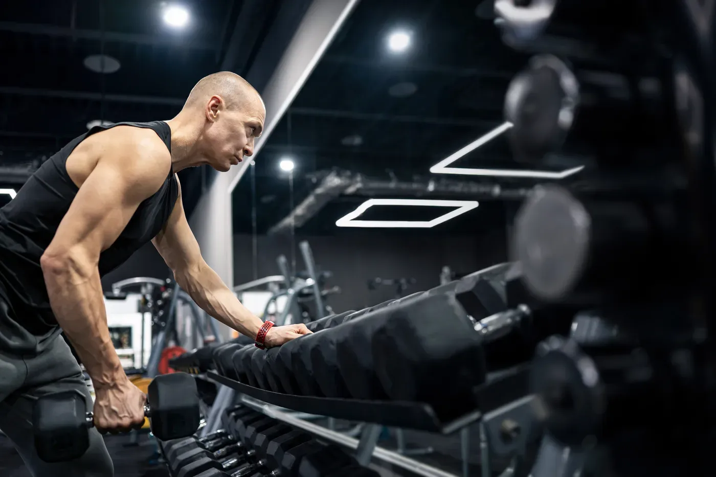 Bald older man doing a dumbbell row at a gym rack