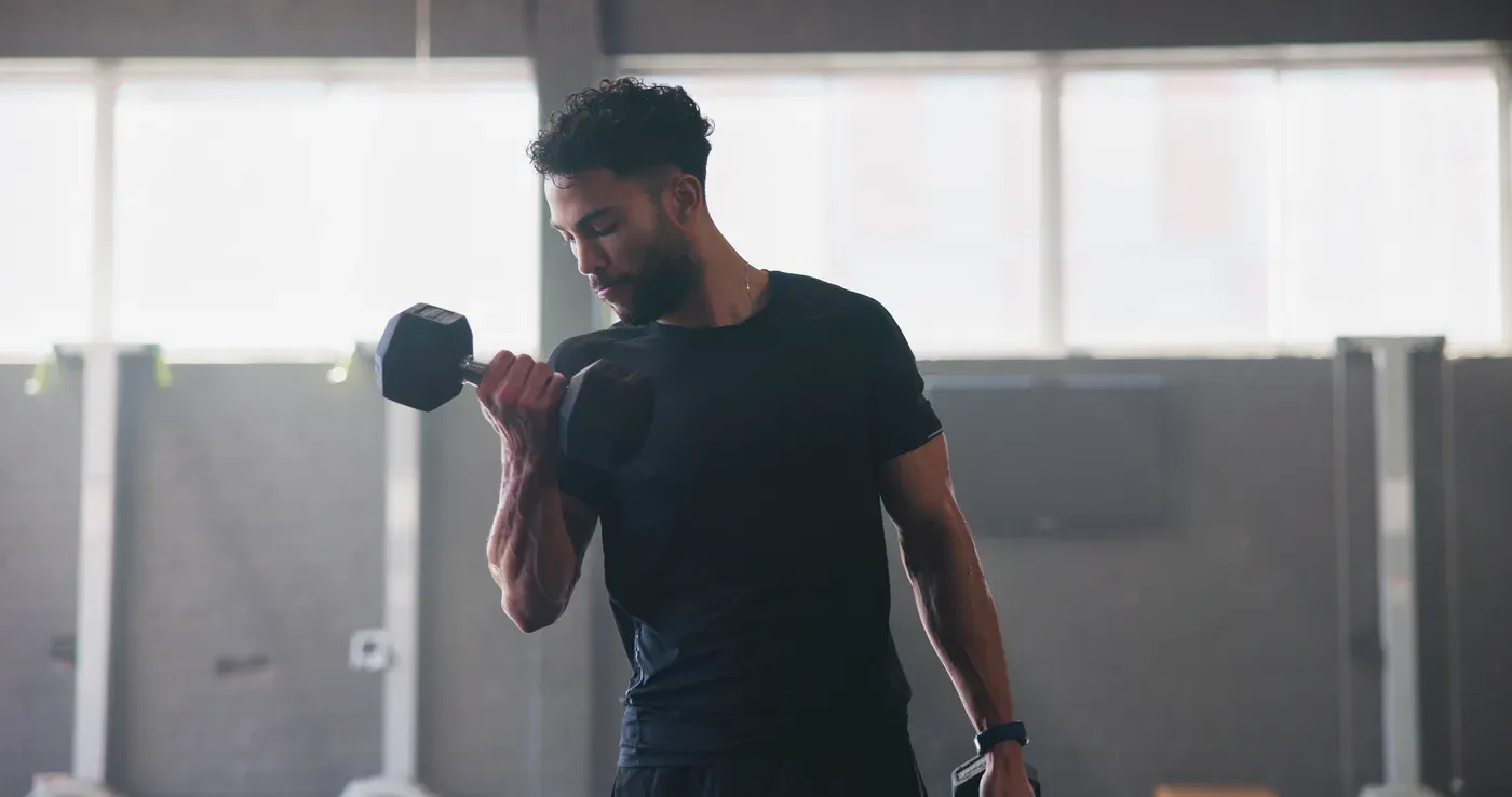 Man doing a single-arm dumbbell curl in a bright gym