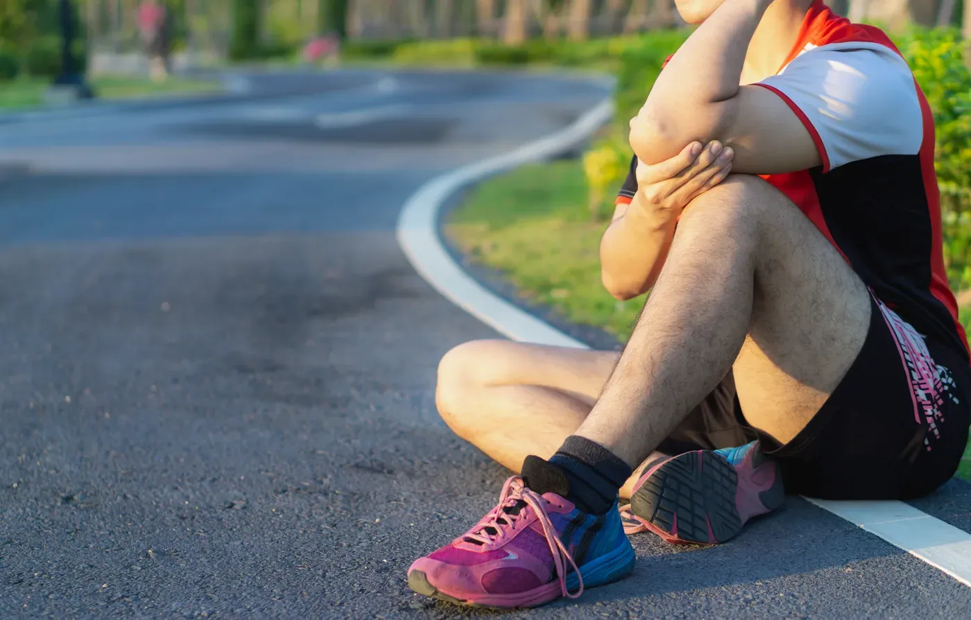 Seated runner holding his sore elbow on a park path