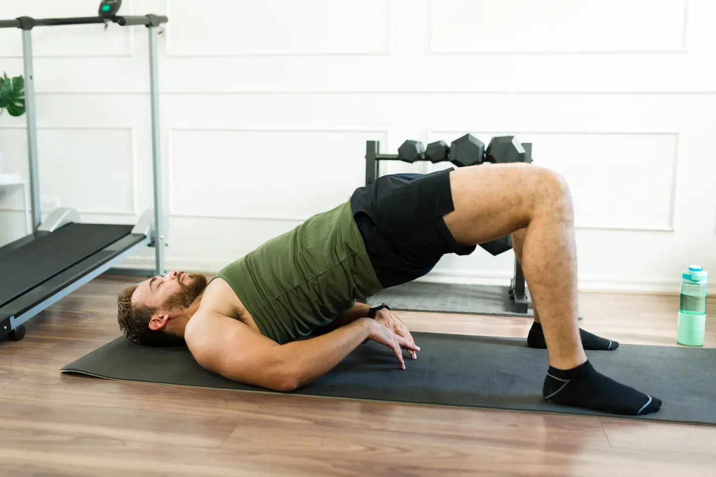Bearded man doing a glute bridge on a mat in a home gym