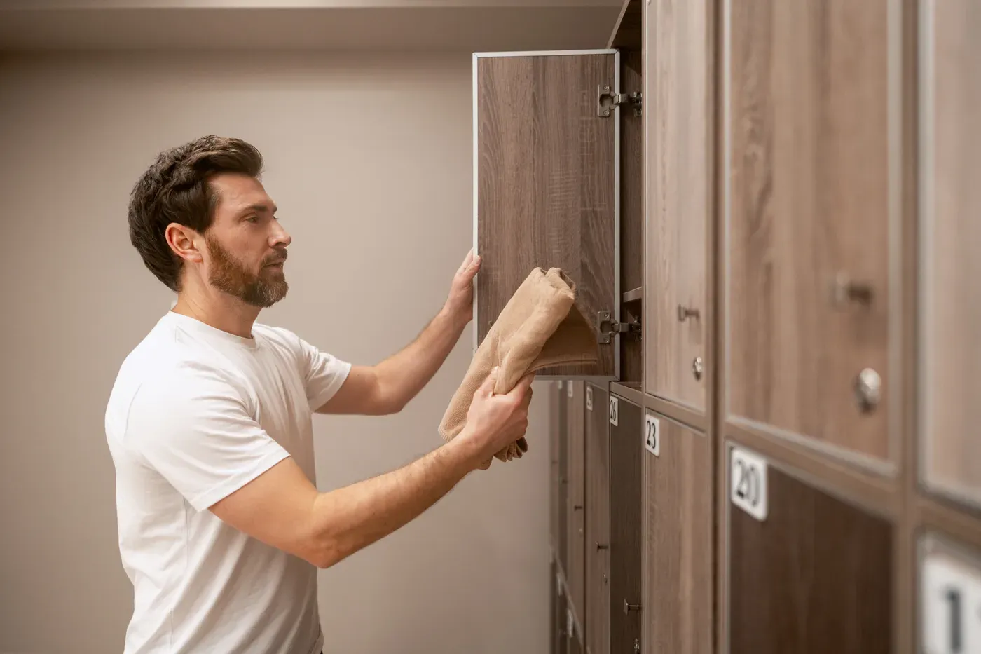 Bearded man placing a towel in a wooden gym locker