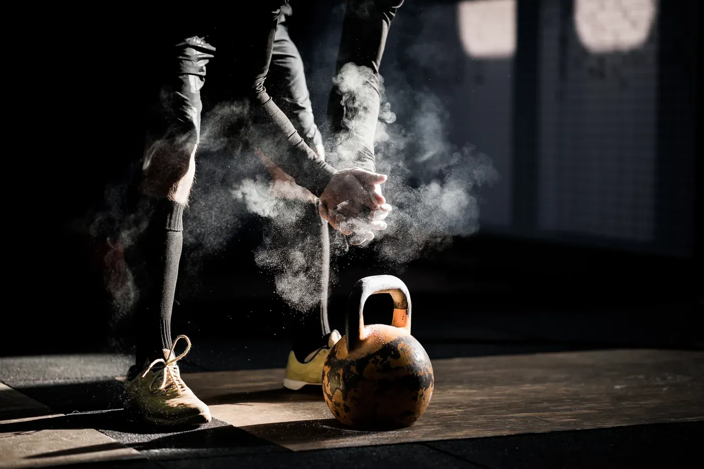 Man chalking his hands above a kettlebell in a dark gym