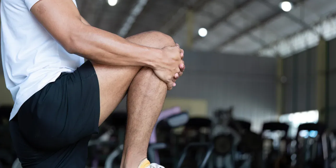 Man in shorts clutching his sore knee inside a gym