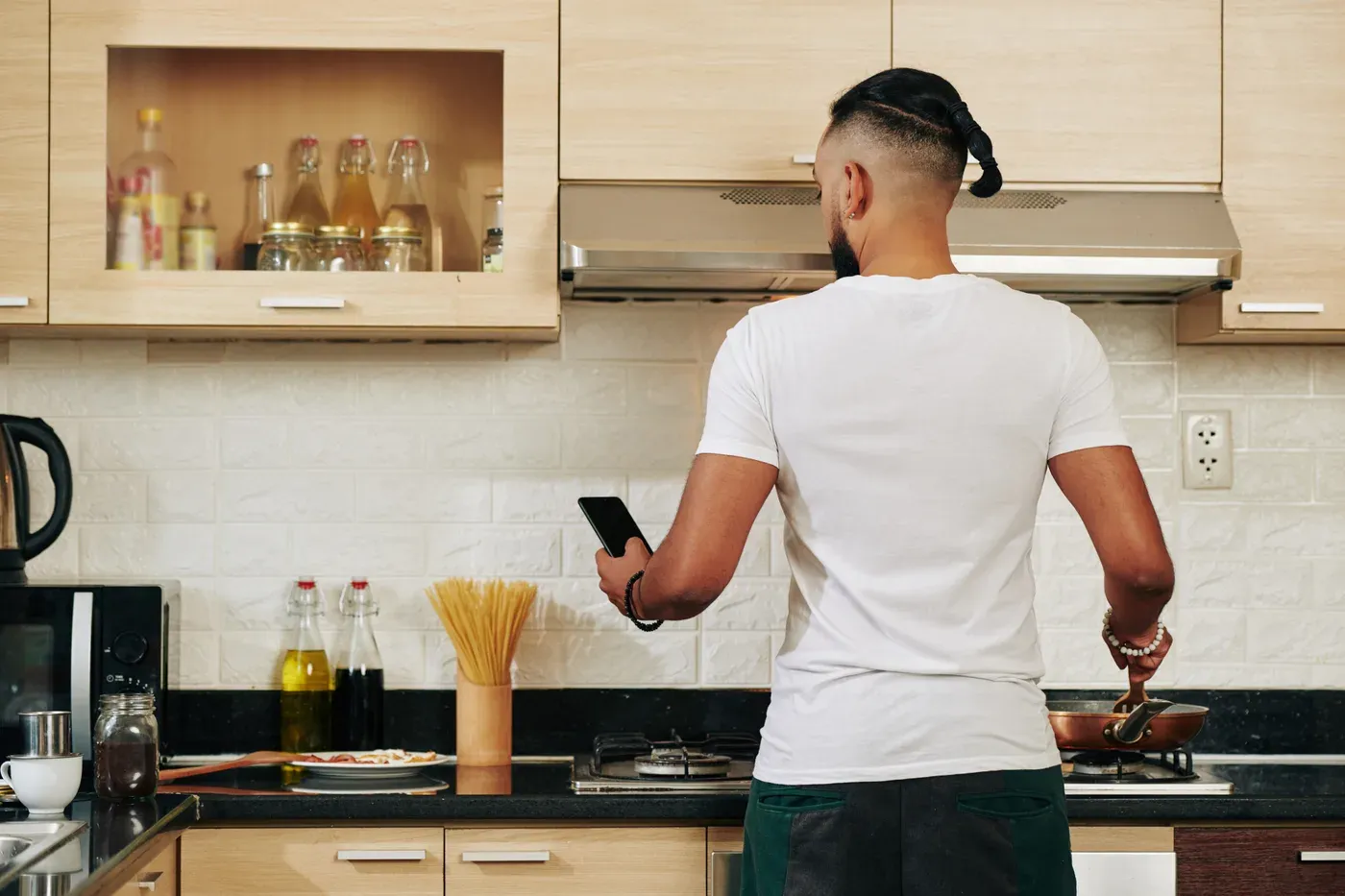 Man cooking breakfast at the stove while checking his phone