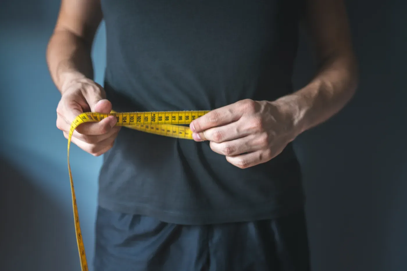 Man measuring his waist with a yellow tape over a dark T-shirt