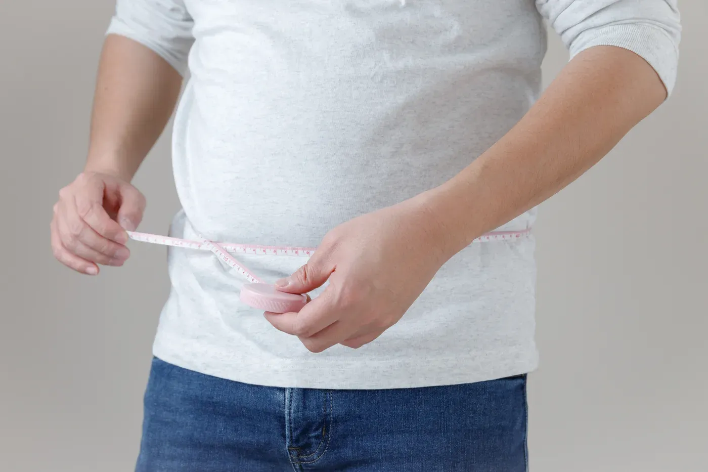 Man in a T-shirt and jeans measuring his waist with a tape