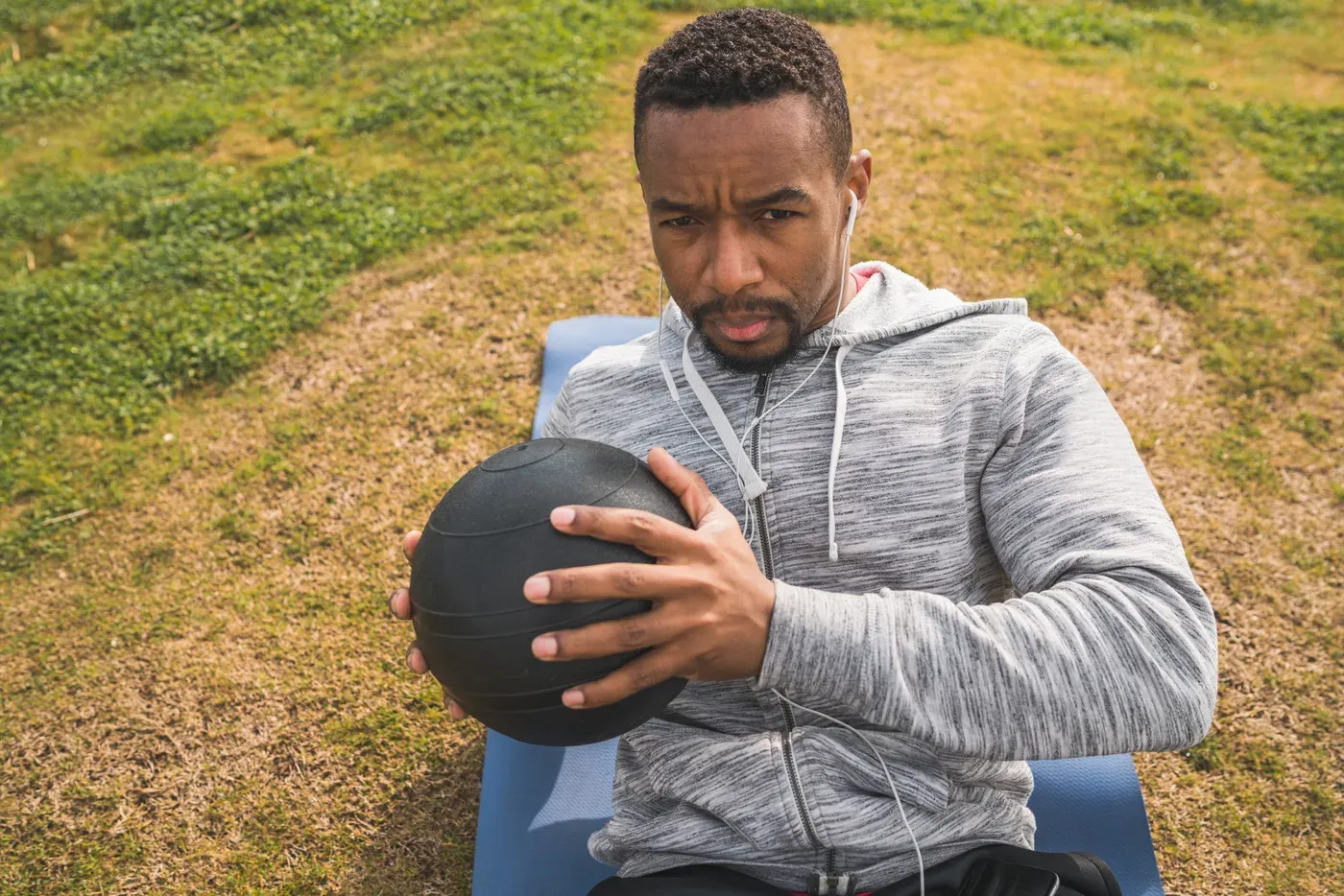 Man doing a medicine ball twist on a mat outdoors