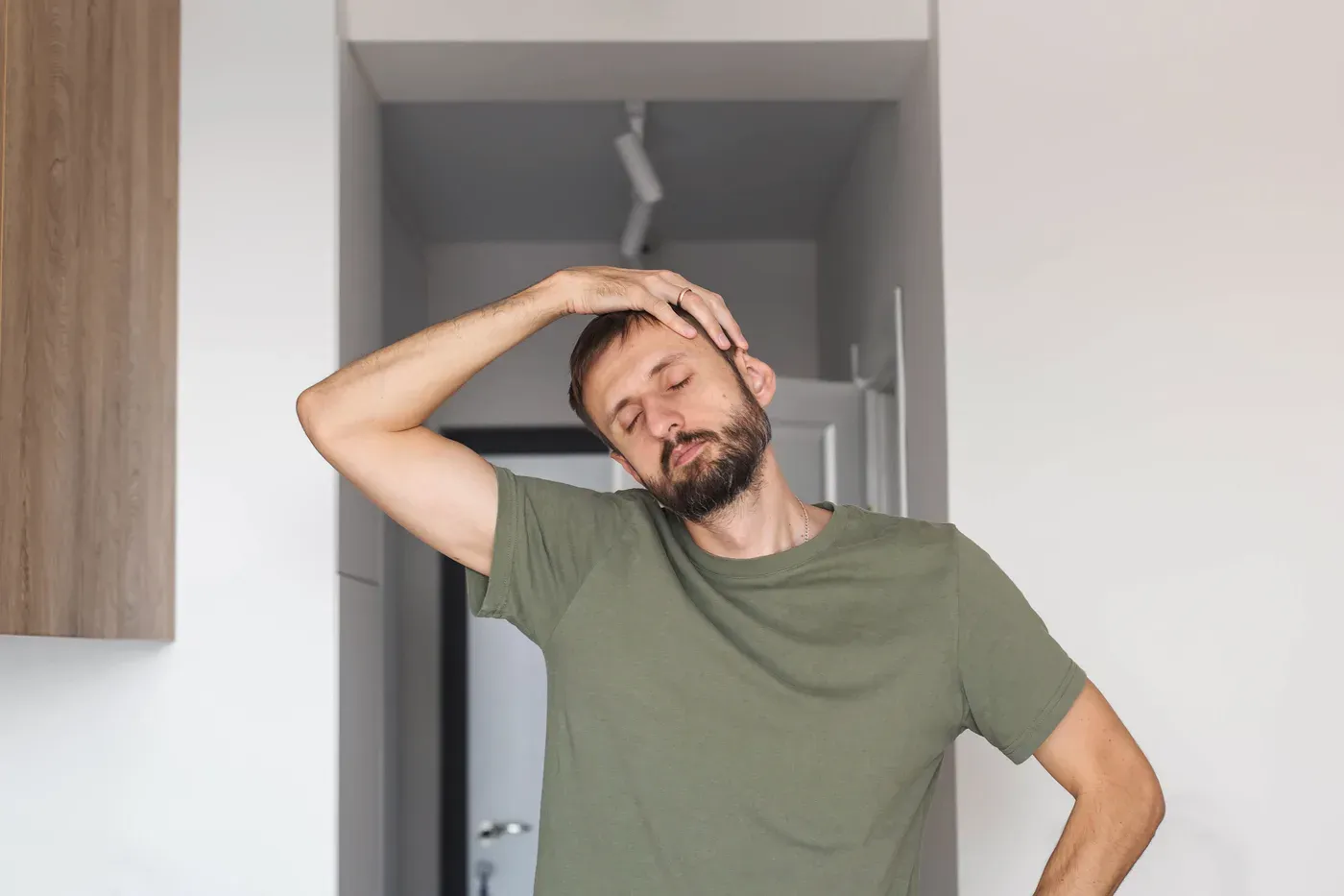 Bearded man stretching his neck to the side with eyes closed at home