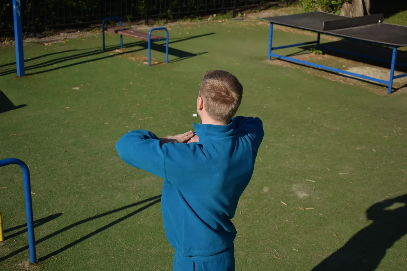 Man in a blue tracksuit warming up his arms at an outdoor fitness park