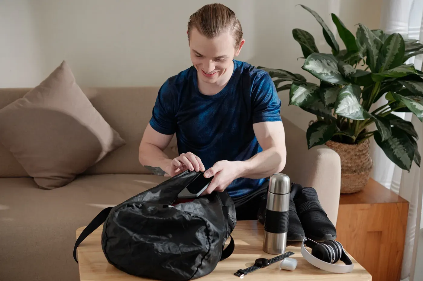 Smiling man packing a gym bag on a coffee table at home