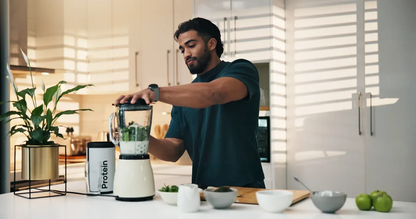 Man blending a protein shake with greens in a bright kitchen