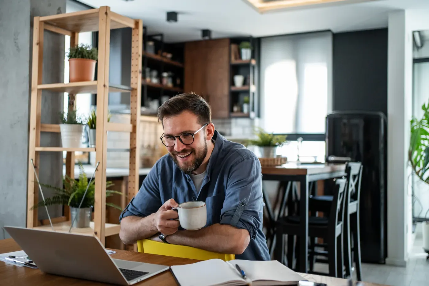 Smiling man in glasses holding a mug at a laptop in a home office