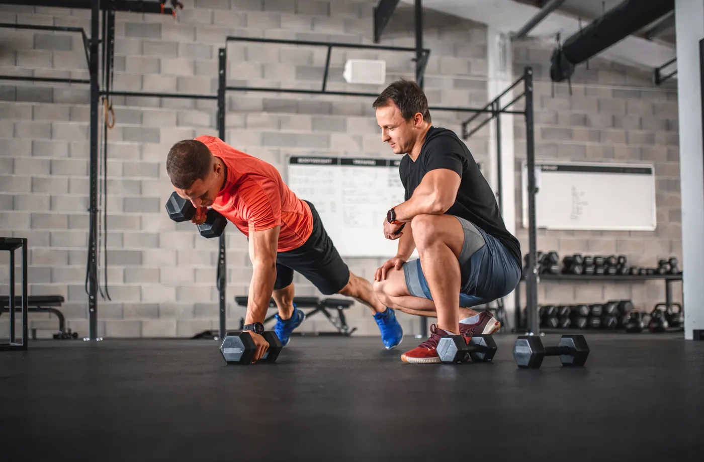 Coach watching a man do a dumbbell renegade row in a gym