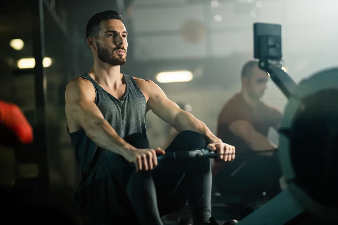 Man working out on a rowing machine in a dim gym