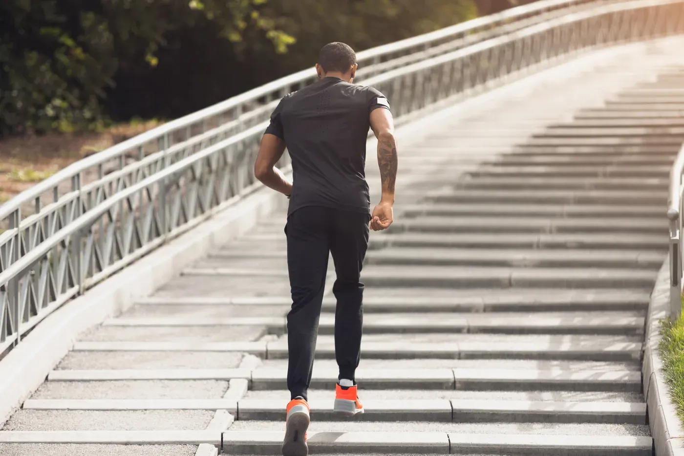 Man in dark training clothes running up a long outdoor staircase