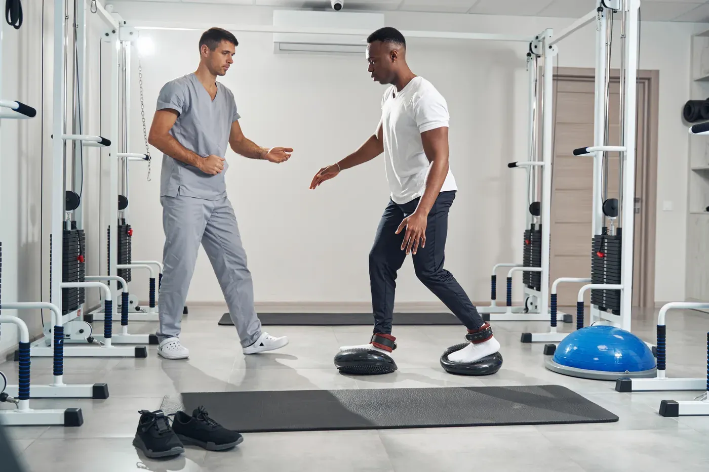 Physiotherapist guiding a man through a balance exercise on stability pads