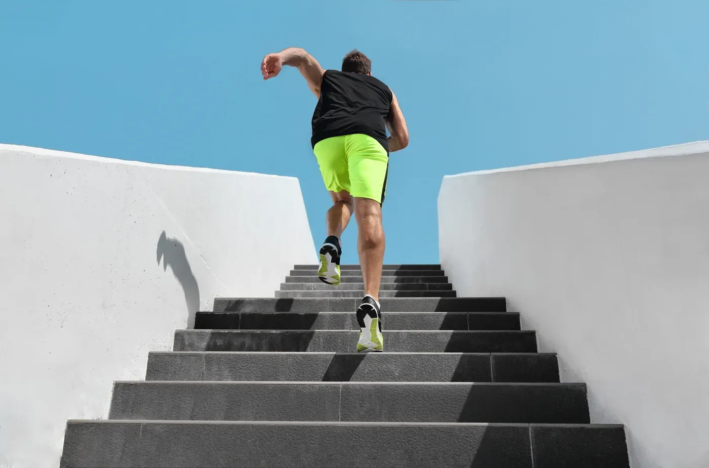 Man sprinting up outdoor concrete stairs under a blue sky